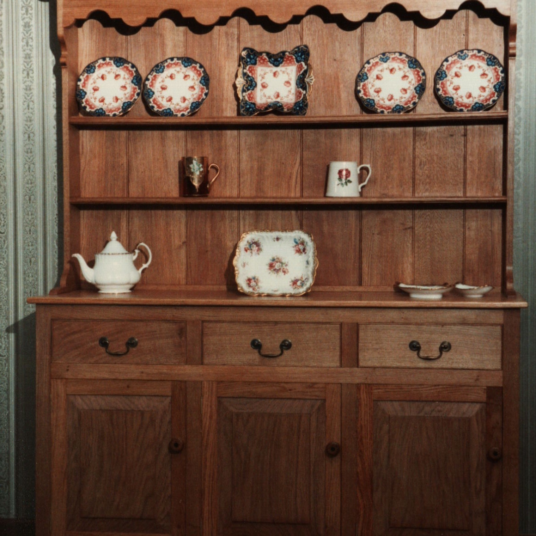 A custom built Welsh dresser made out of mahogany with decorative plates, cups and teapot.